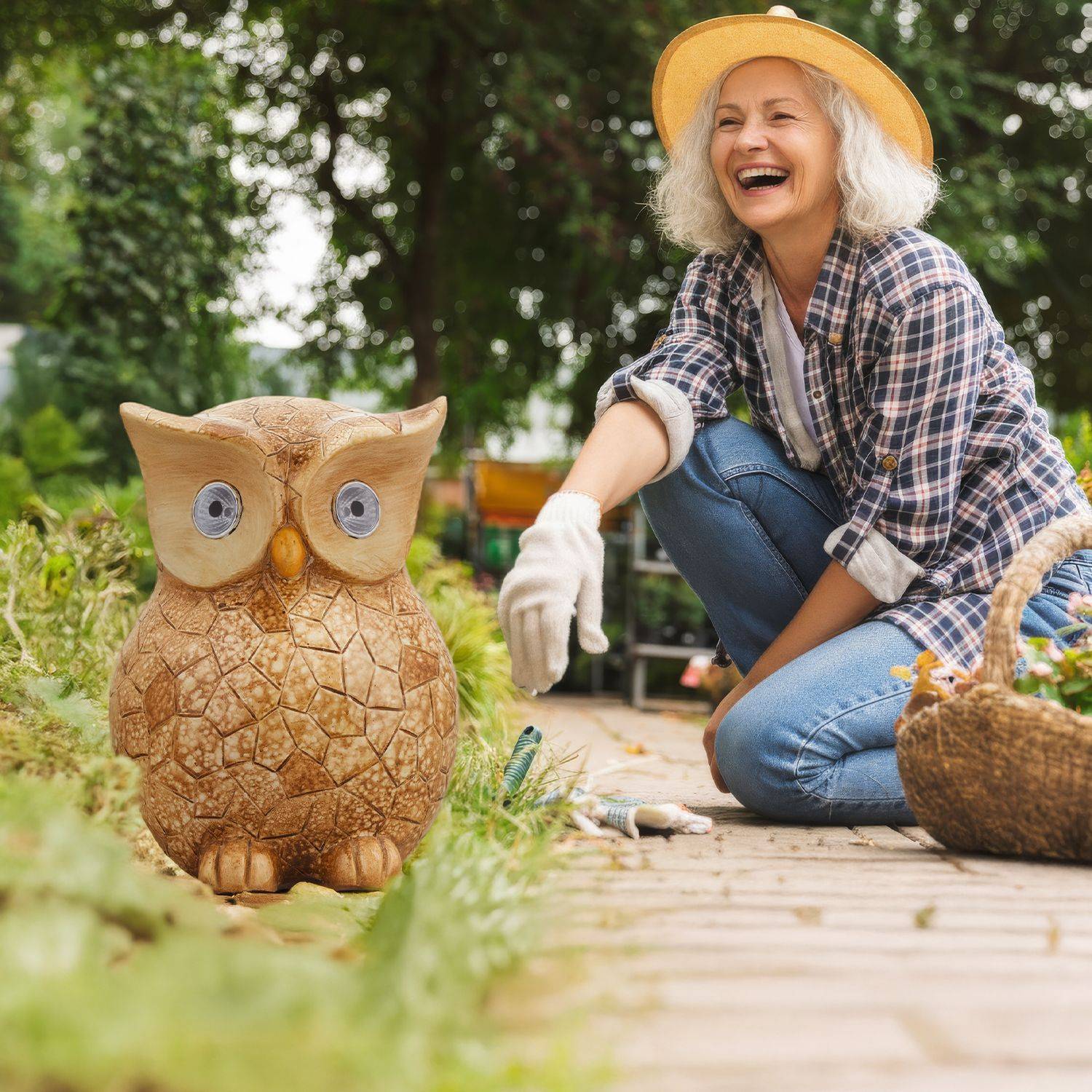 Frau in kariertem Hemd und Jeans hockt im Garten neben einer großen Eulenfigur aus Stein und einem Korb mit Gartenwerkzeugen