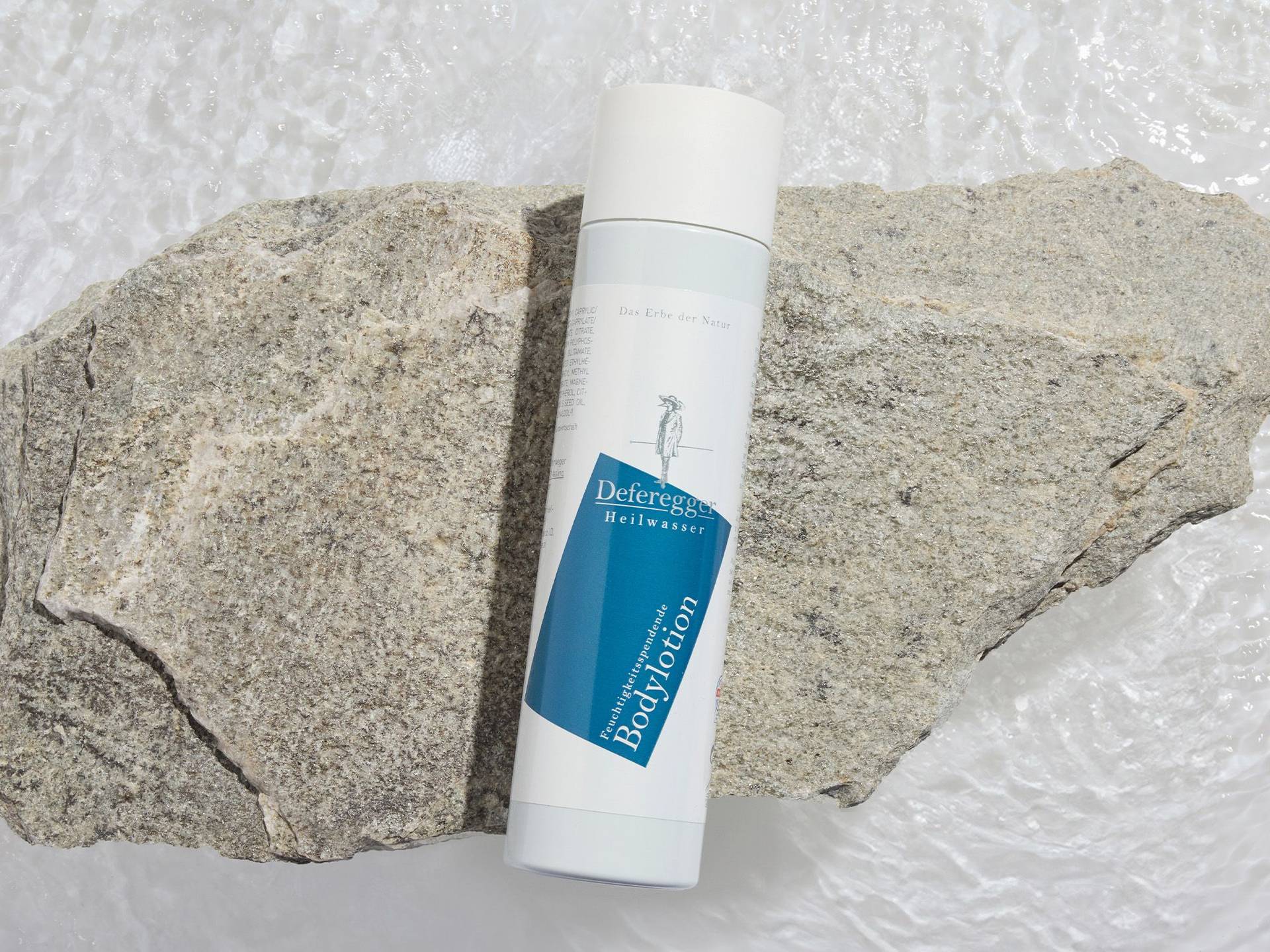 Bodylotion für trockene und sensible Haut Weiße Flasche mit blauem Etikett und Aufschrift "Deferegger Heilwasser Bodylotion" liegt auf zwei großen grauen Steinen