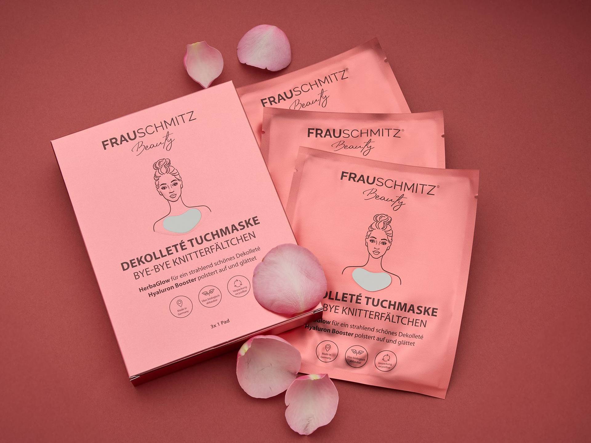 Verpackung und drei einzelne Sets der FRAUSCHMITZ Beauty Dekolleté Tuchmaske, rosa, mit stilisierter Rückenansicht einer Frau und Rosenblättern auf rotem Untergrund.