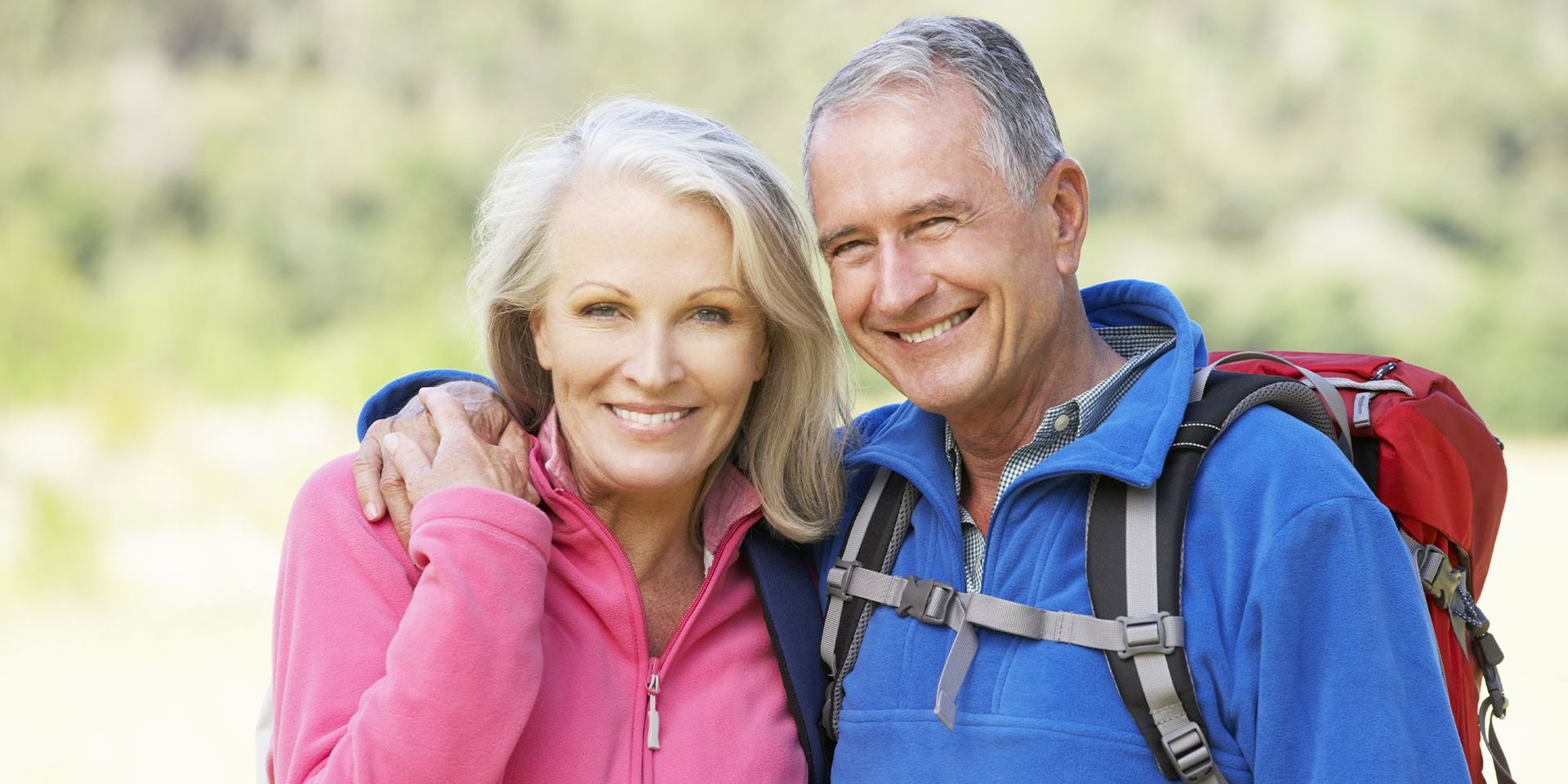 Älteres Paar in Outdoor-Kleidung lächelt in die Kamera, Frau in pinker Jacke, Mann in blauer Jacke.