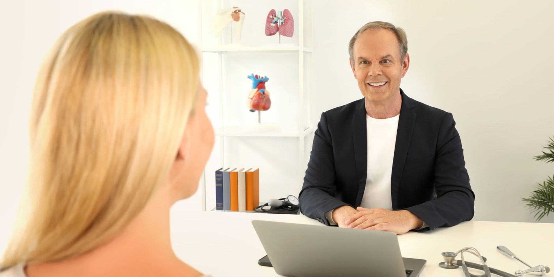 Der Experte Winfried in einer Beratung mit einer blonden Kunden an einem gemeinsamen Tisch vor einem aufgeklappten Laptop.