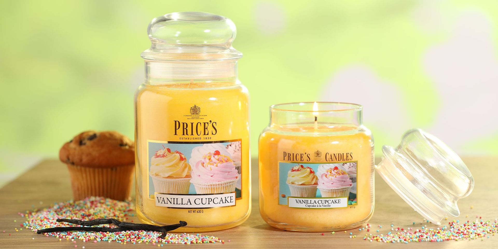 Zwei Vanille-Cupcake-Duftkerzen von Price's Candles auf einem Holztisch mit bunten Streuseln