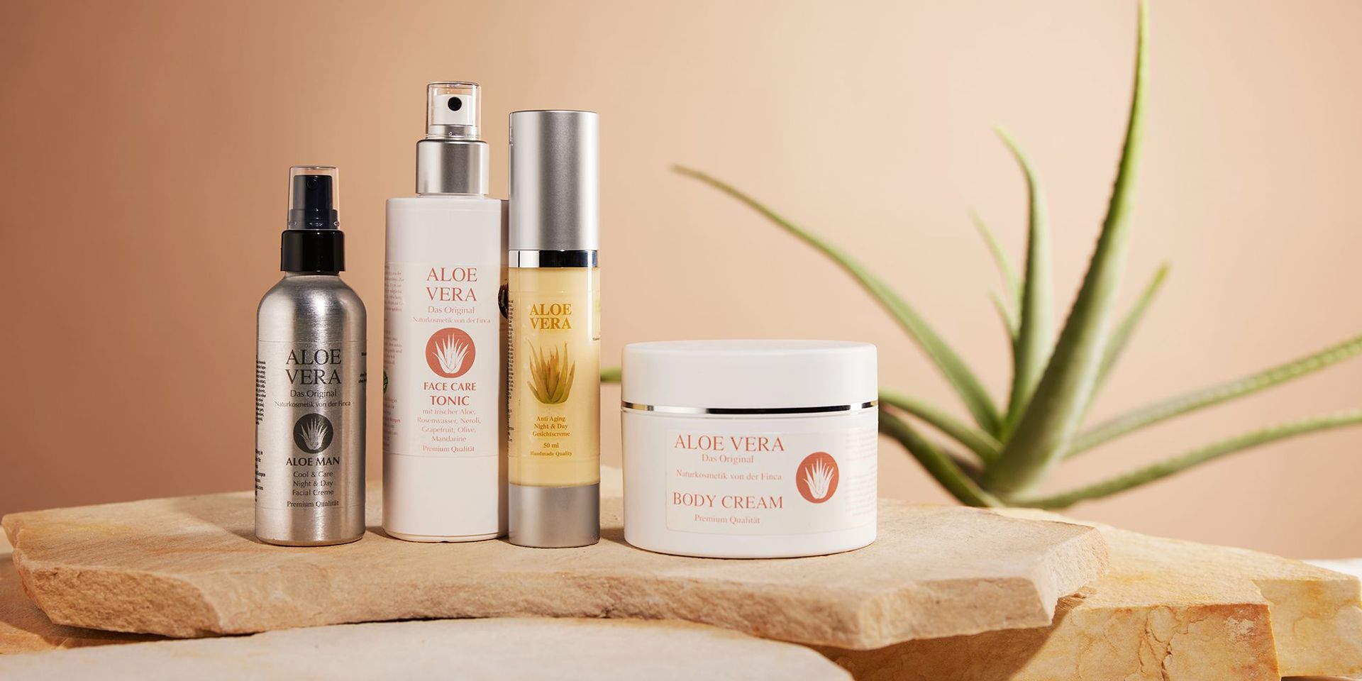 Ausgewählte Produkte von Aloe Finca auf einem beigen Sandstein vor einer Aloe Vera Pflanze.