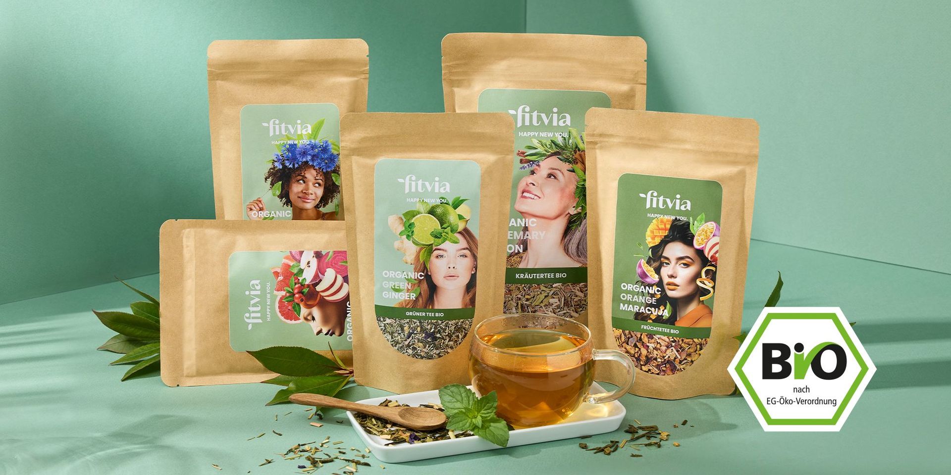 Fitvia Bio-Tee-Packungen mit Teetasse auf weißem Tablett, umgeben von grünen Blättern