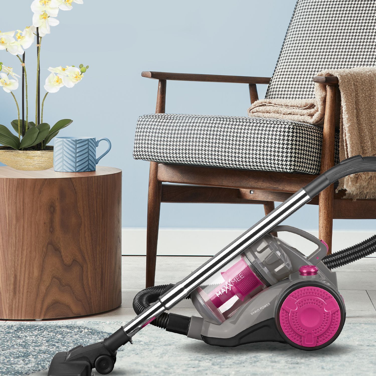 Staubsauger mit pinken Akzenten neben einem Sessel und Holztisch im Wohnzimmer