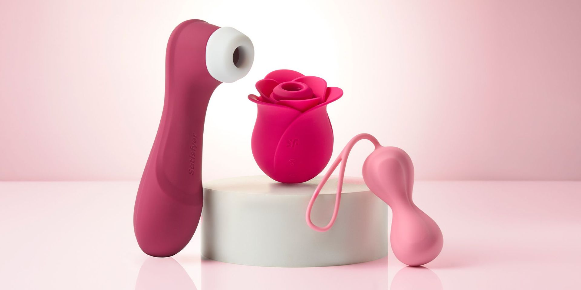 Drei Produkte von Satisfyer auf einem hellpinken Hintergrund 