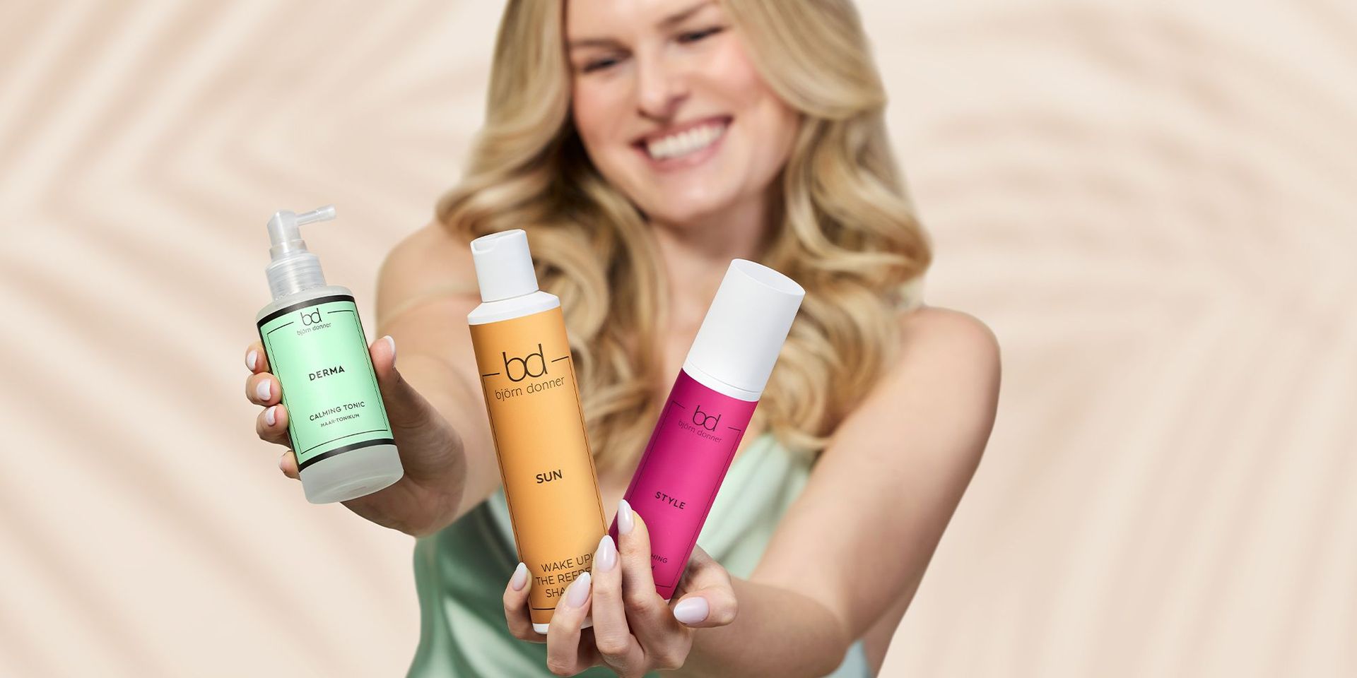 Frau hält drei Björn Donner Haarpflegeprodukte: grünes 'Derma Calming Tonic', orangefarbenes 'Sun Wake Up The Beach Shampoo' und pinkes 'Style' Spray