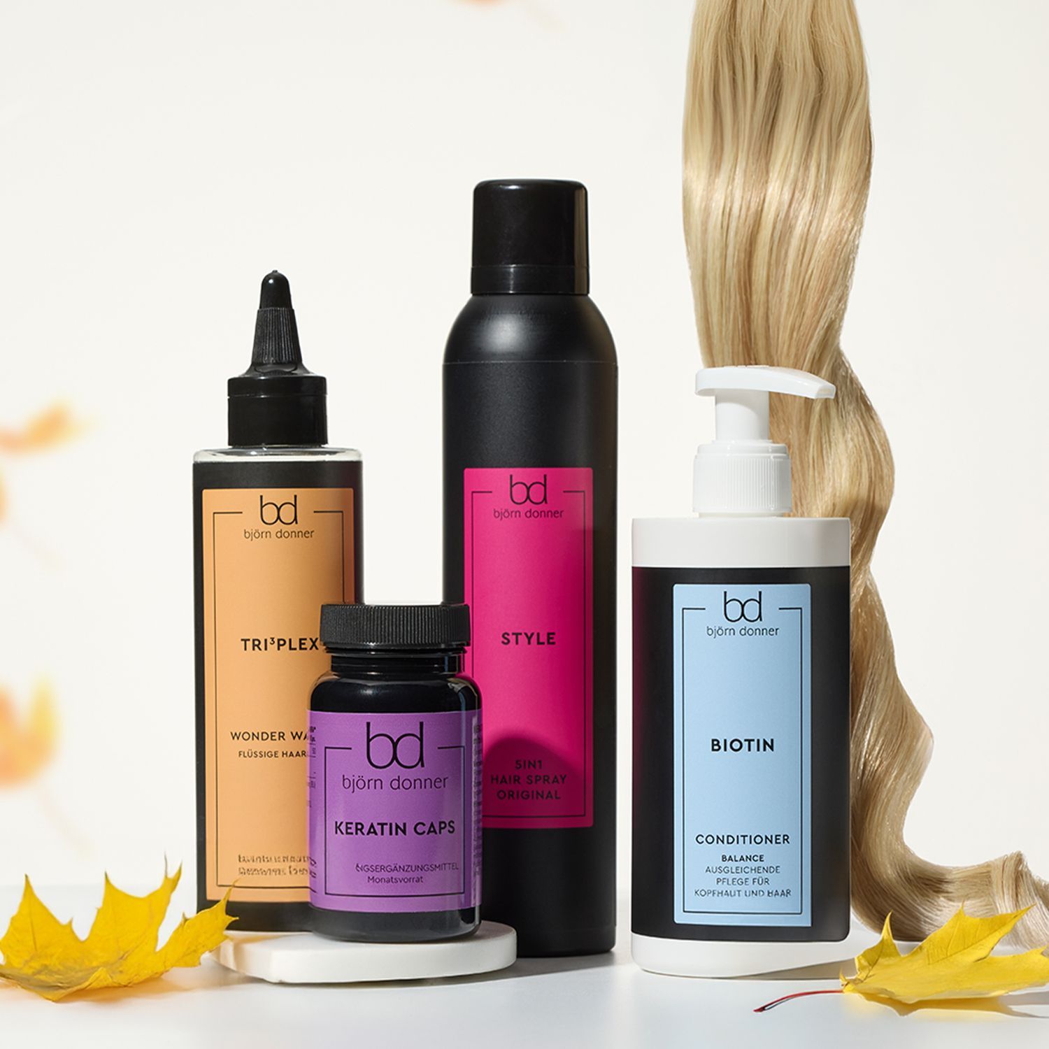 Vier Haarpflegeprodukte von Björn Donner: Triplex Wonder Water, Keratin Caps, Style Hair Spray, Biotin Conditioner neben einer blonden Haarsträhne und Herbstblättern