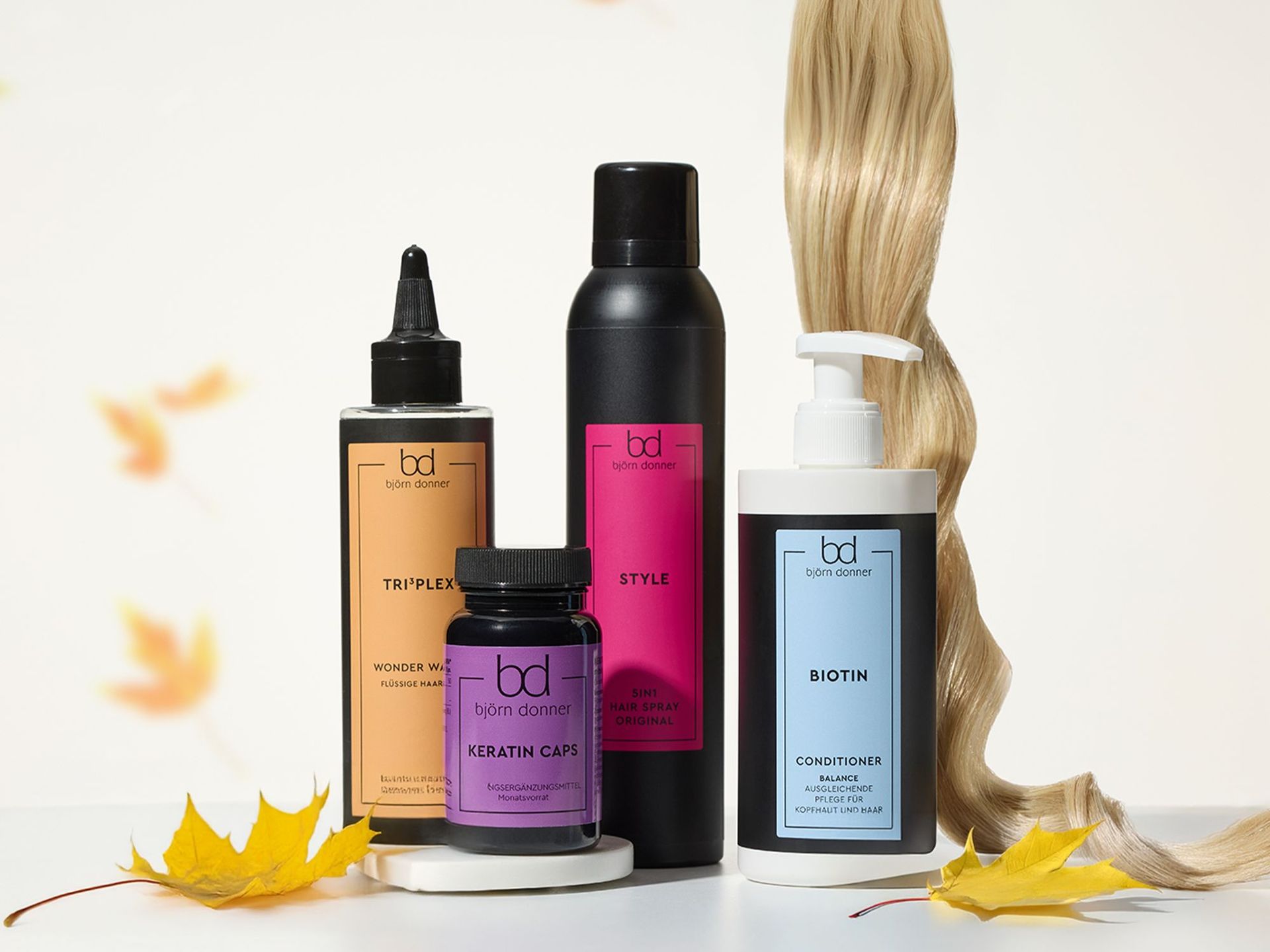 Vier Haarpflegeprodukte von Björn Donner: Triplex Wonder Water, Keratin Caps, Style Hair Spray, Biotin Conditioner neben einer blonden Haarsträhne und Herbstblättern