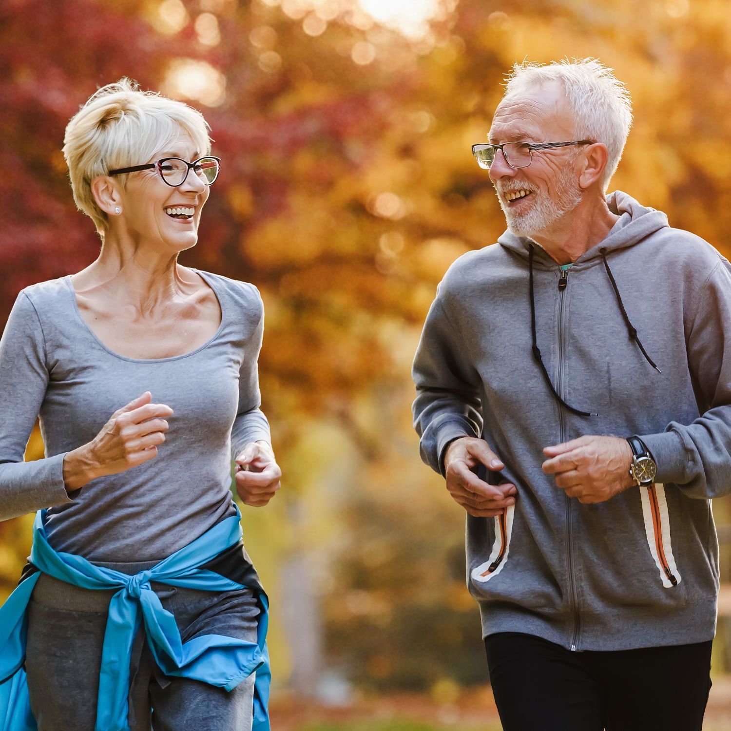 Zwei ältere Menschen, eine Frau und ein Mann, beim Joggen im Herbst.