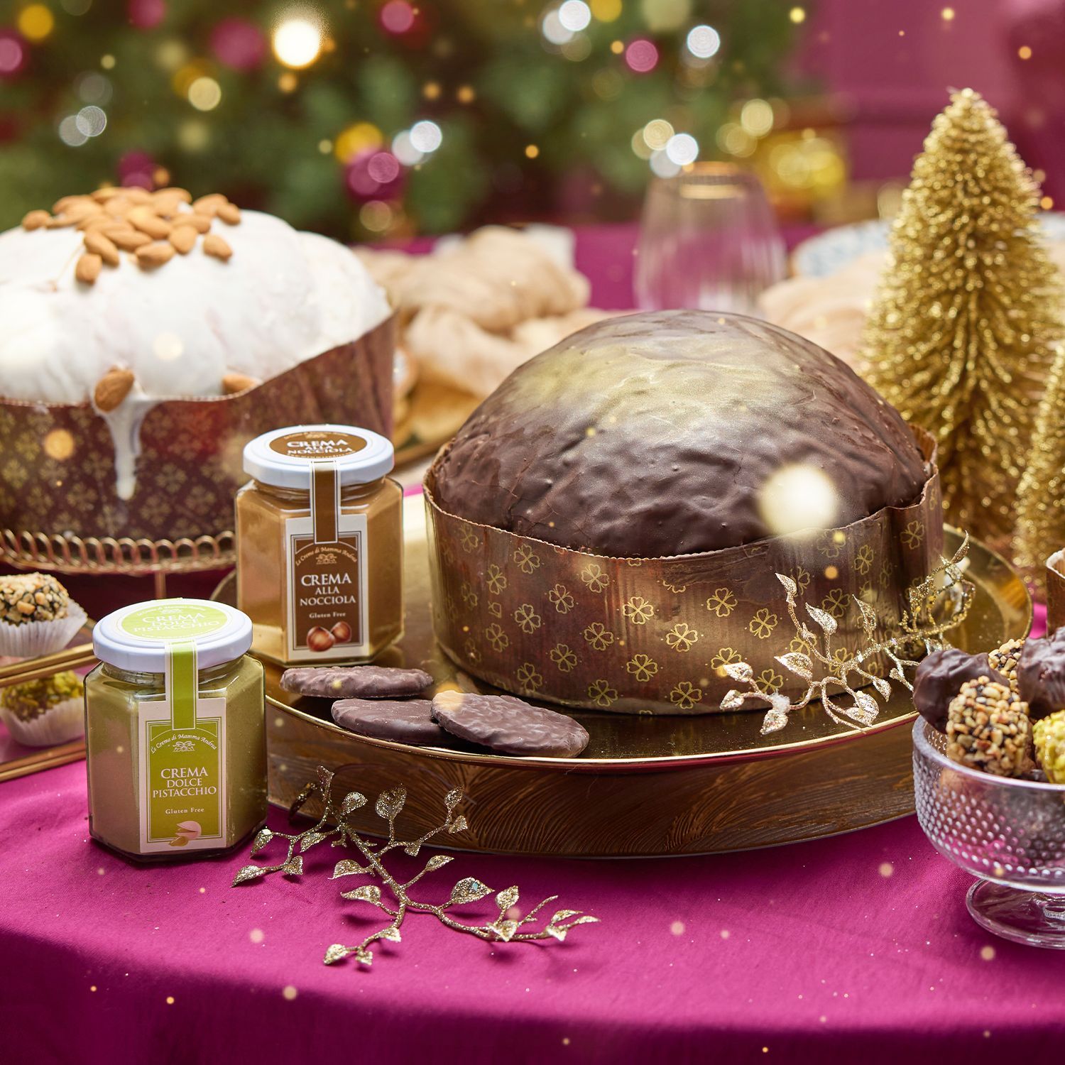 Drei Panettone mit Zuckerguss und Nüssen, Schokoladenkugel, Pralinen, Marmeladengläser und goldene Weihnachtsdekoration auf Holztisch.