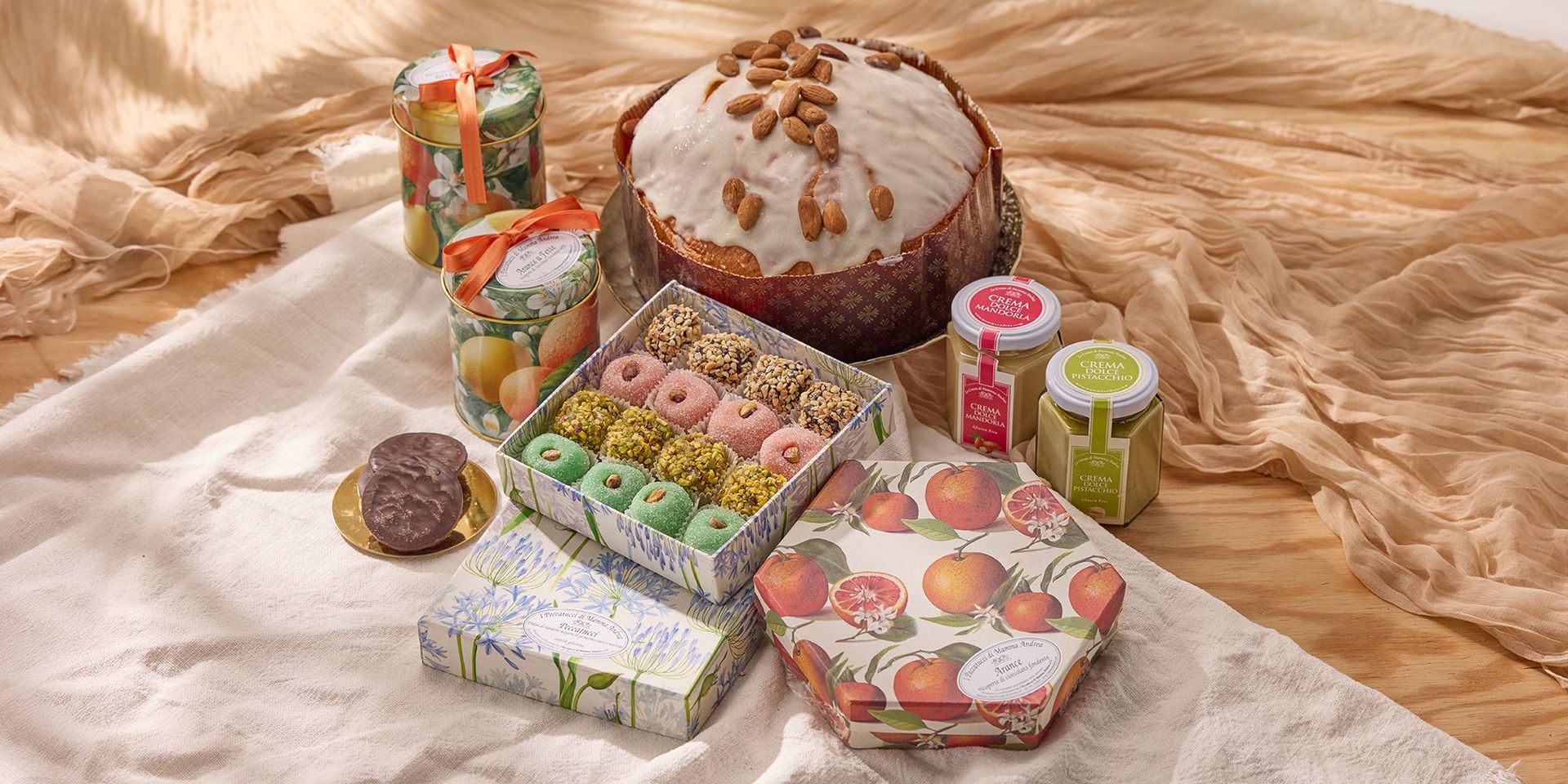 Großer runder Kuchen mit Zuckerguss und Mandeln, daneben bunte Pralinen in Schachteln, zwei Gläser mit Aufklebern und zwei kleine Gläser mit Aufstrichen.