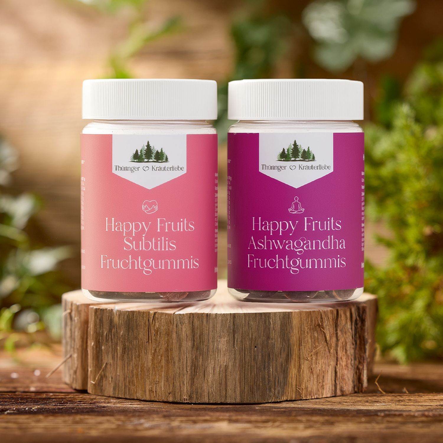 Zwei Produkte von Thüringer Kräuterliebe mit weißen Deckeln und bunten Etiketten stehen auf einem Holzstamm, im Hintergrund unscharfe grüne Pflanzen