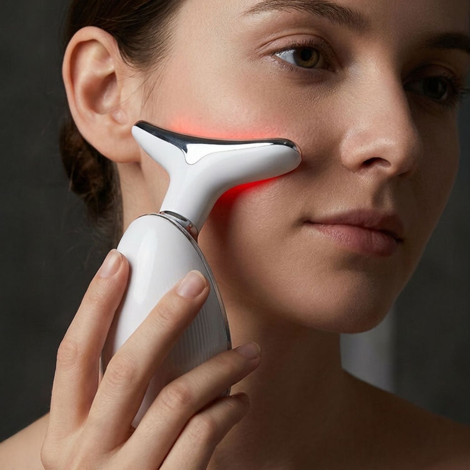 Frau hält ein weißes LED-Massagegerät mit T-förmigem Kopf an ihre rechte Wange