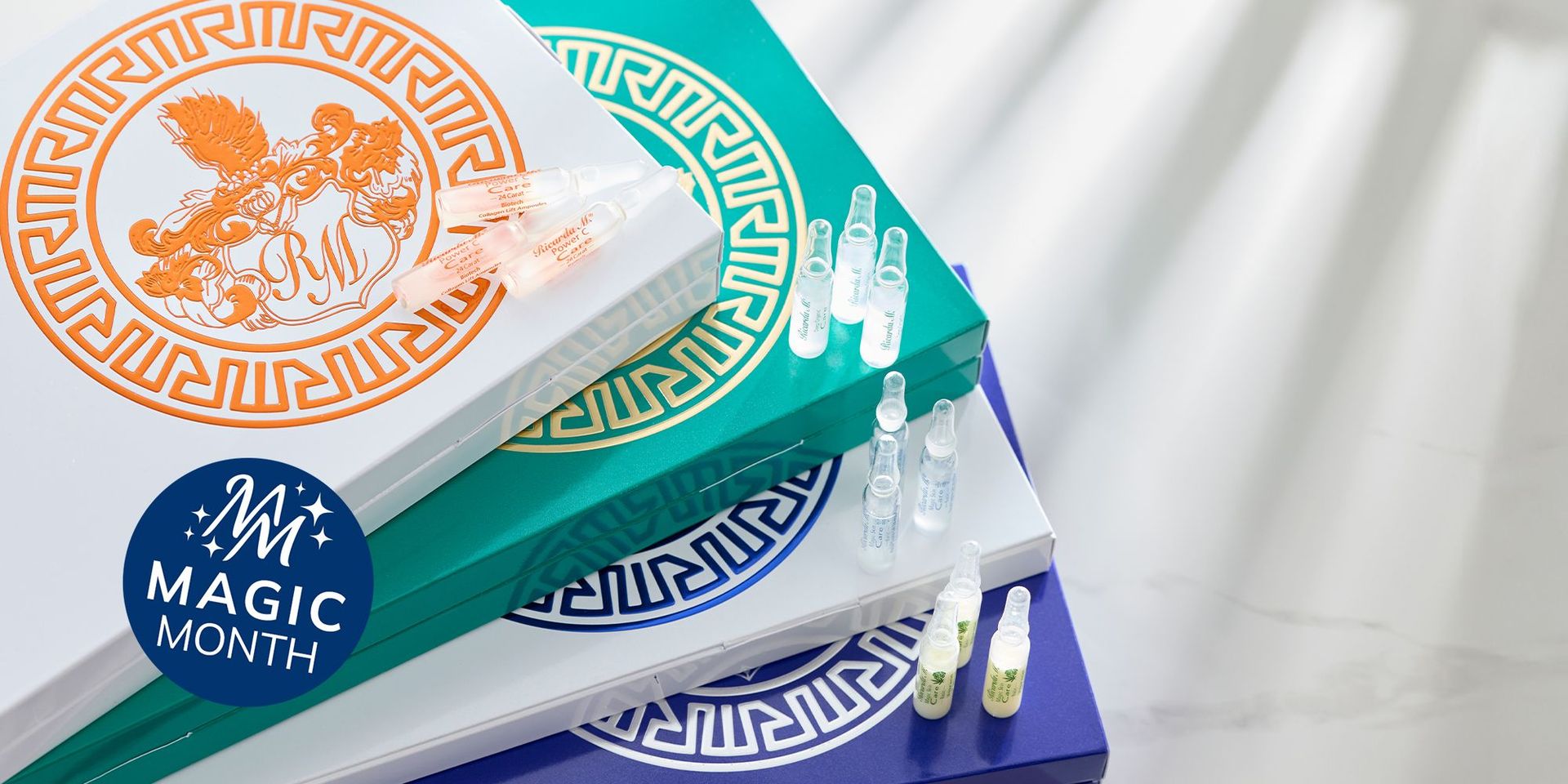 Mehrere gestapelte, rechteckige Verpackungen mit dekorativen Mustern und kleinen durchsichtigen Ampullen darauf