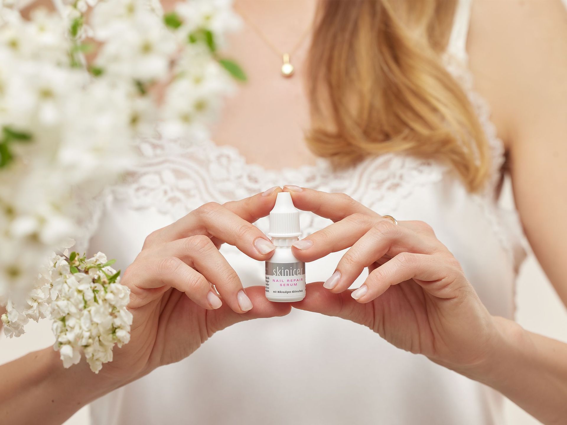 Frau in weißer Bluse hält kleine weiße Flasche mit Aufschrift 'skinicer NAIL REPAIR SERUM' zwischen den Fingern