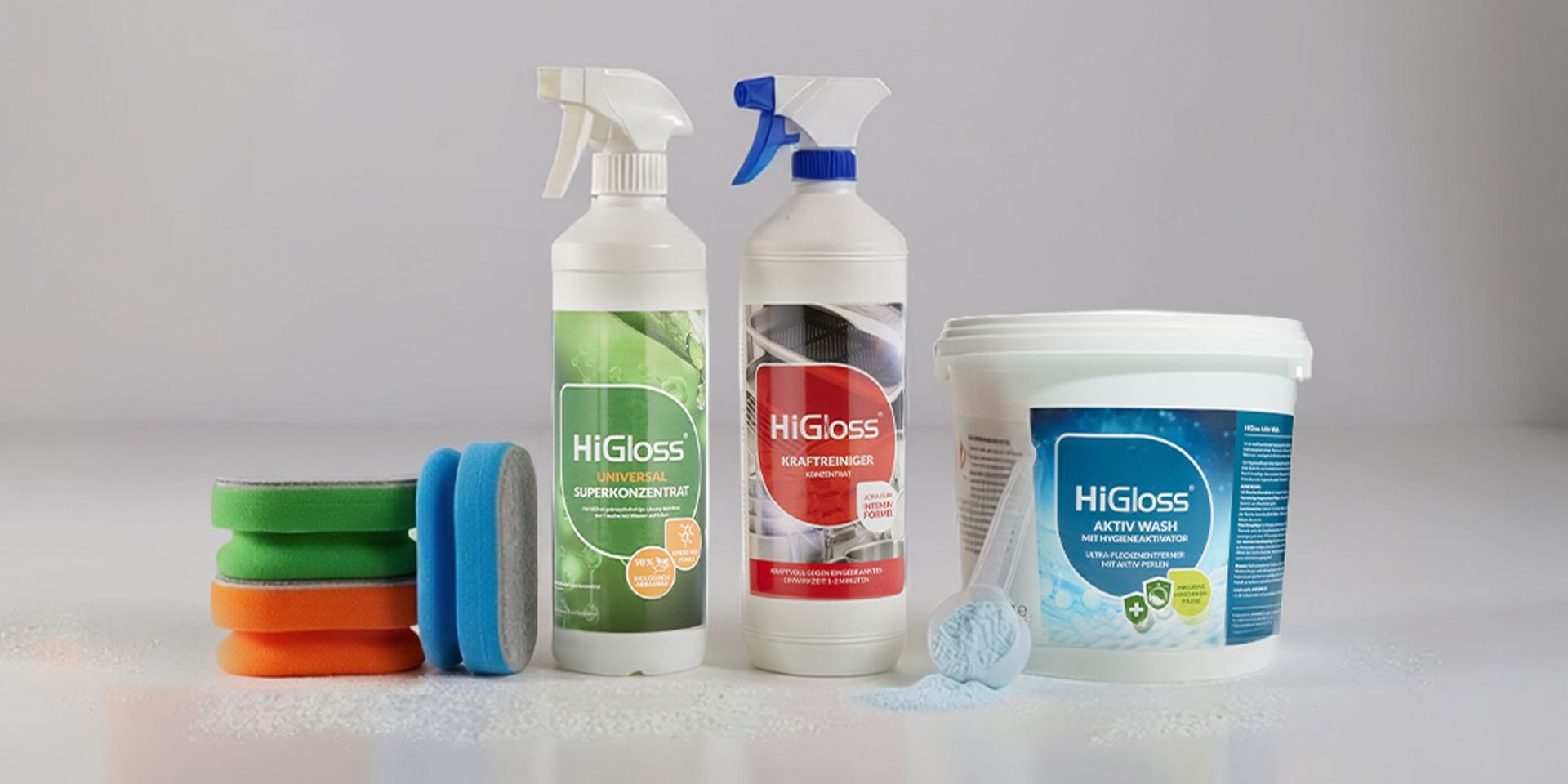 Mehrere bunte Reinigungsschwämme, zwei Sprühflaschen mit HiGloss-Labels und ein Eimer mit Bürste, alle auf hellem Untergrund
