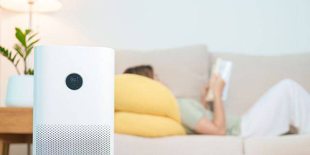 Chronische Bronchitis – Tipps für den Alltag Frau liegt lesend auf dem Sofa, im Vordergrund steht ein Luftreinigungsgerär