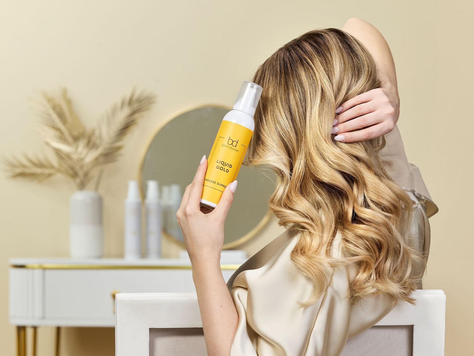 Luxuspflege für Ihr Haar! Junge Frau mit langen blonden, gewellten Haaren hält in der Hand ein Produkt von Liquid Gold