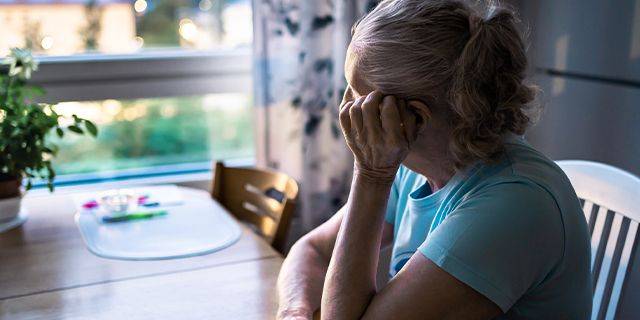 Depression im Alltag Ältere Frau sitzt nachdenklich am Tisch und schaut aus dem Fenster