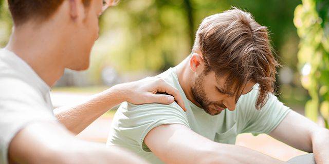 Sucht-Betroffenen wird geholfen Ein Mann mit hellgrünem T-Shirt sitzt mit gesenktem Kopf, während eine andere Person ihm tröstend auf die Schulter legt.