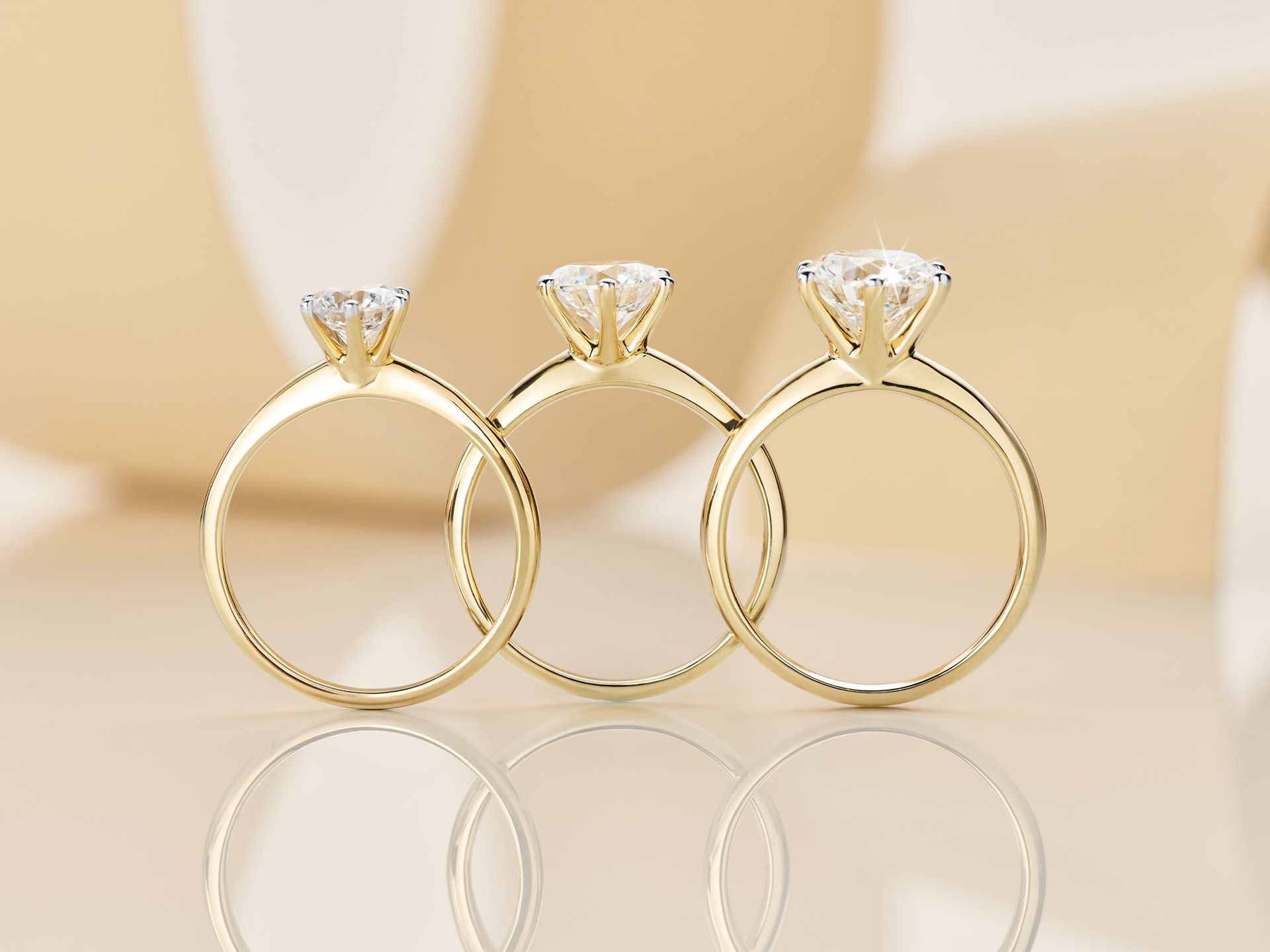 Diamantringe bis zu 3,0 Karat Drei Diamant-Solitärringe aufgestellt nebeneinander auf einem hellgelben Hintergrund