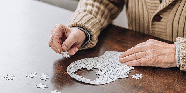 Alzheimer Ältere Person setzt ein Puzzleteil in ein Puzzle in Form eines menschlichen Kopfes, symbolisch für Alzheimer