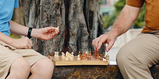 Schach spielen Zwei Personen spielen Schach an einem Holztisch im Freien vor einem Baum