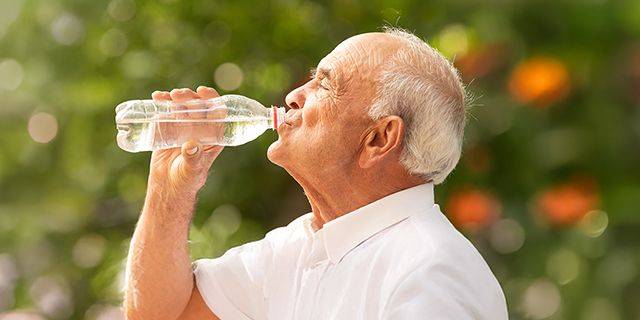 Hitze Älterer Mann trinkt Wasser aus einer Plastikflasche im Freien
