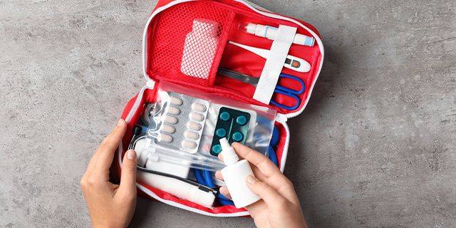 Reiseapotheke Offene rote Reisapotheke mit Medikamenten, Thermometer, Schere und Desinfektionsspray in Händen