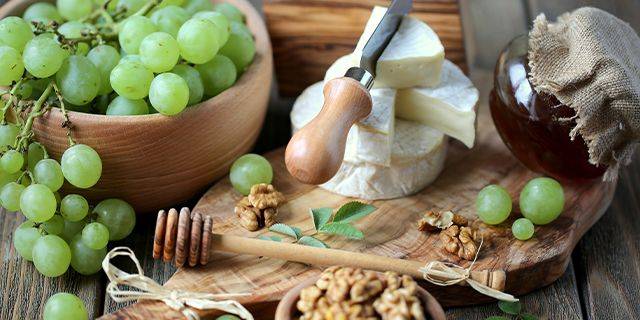 Weintrauben Platte Grüne Trauben in einer Holzschüssel, daneben ein Holzbrett mit Käse, einem Messer, Honig im Glas und Walnüssen.