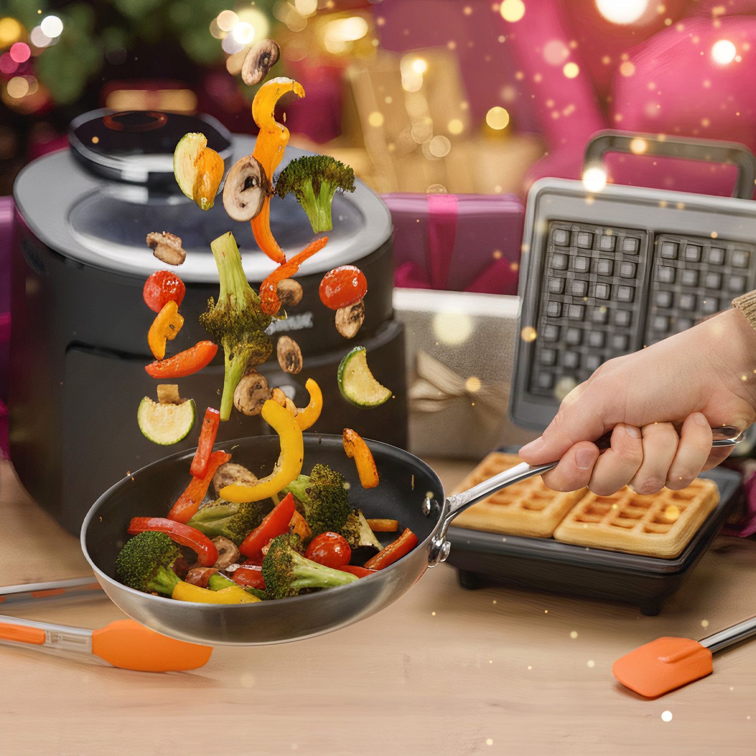 Zubereitung & Küchenhelfer Hand hält Pfanne mit springendem Gemüse wie Brokkoli, Pilzen, Paprika und Kirschtomaten in einer Küche mit Waffeleisen im Hintergrund.