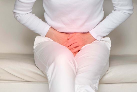 Ausschnitt einer sitzenden Frau in weißer Kleidung, die sich ihr Becken hält. Dieses leuchtet ein wenig rot, was Beckenboden-Schmerzen indizieren soll.