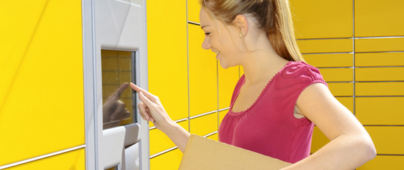 Junge Frau mit Paket in der Hand bedient eine DHL Packstation